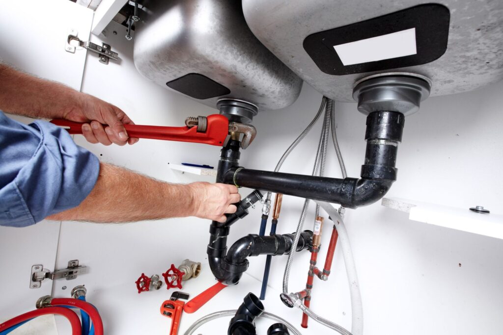 Plumber repairing drain pipes beneath a kitchen sink in Lake Elsinore